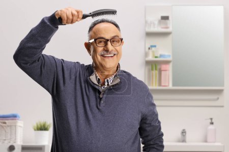 Photo for Mature man with a hair brush smiling in a bathroom - Royalty Free Image
