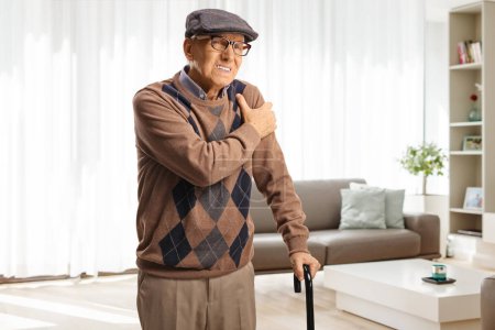 Photo for Elderly man in pain holding shoulder at home in a living room - Royalty Free Image