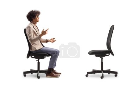 Téléchargez les photos : Plan du profil d'un homme parlant et assis dans une chaise de bureau en face d'une chaise vide isolée sur fond blanc - en image libre de droit