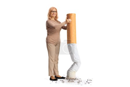 Téléchargez les photos : Femme d'âge moyen éteignant une grosse cigarette et souriant isolé sur fond blanc - en image libre de droit