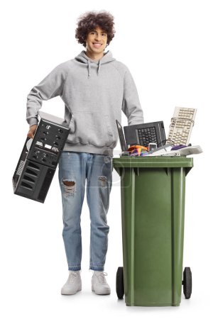 Foto de Joven lanzando una vieja computadora y de pie junto a un contenedor con desechos electrónicos aislados sobre fondo blanco - Imagen libre de derechos
