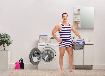 Photo for Full length portrait of a young man in underwear holding a laundry basket full of clothes in a bathroom - Royalty Free Image