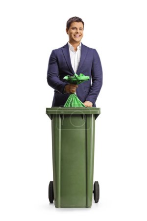 Photo for Full length portrait of a smiling young man throwing a waste bag in a garbage bin isolated on white background - Royalty Free Image