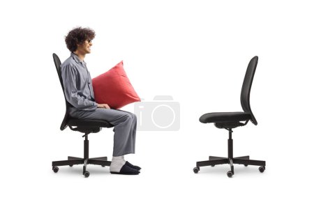 Perfil de un hombre en pijama sentado y mirando una silla de oficina vacía aislada sobre fondo blanco