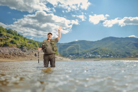 Foto de Pescador con una caña de pescar de pie y saludando en un lago - Imagen libre de derechos