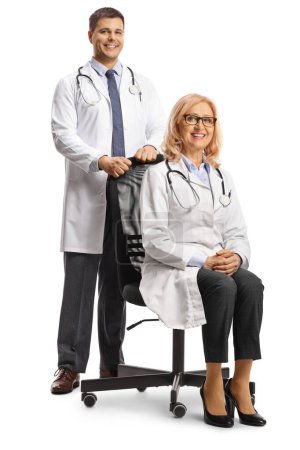 Photo for Male doctor standing behind a female doctor seated in an office chair isolated on white background - Royalty Free Image