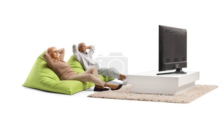 Photo for Middle aged woman resting on green bean bag armchair next to a young african american man in front of tv - Royalty Free Image