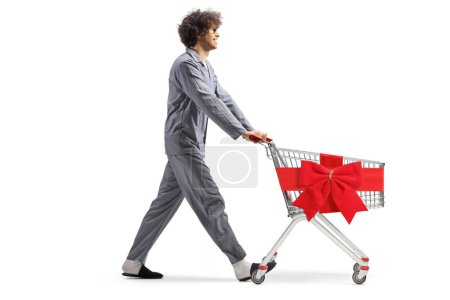 Photo for Young man in pajamas walking with a shopping cart tied with a red ribbon isolated on white background - Royalty Free Image