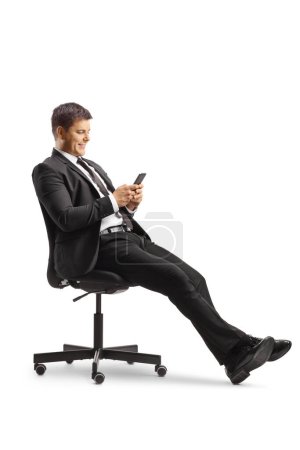 Téléchargez les photos : Homme d'affaires assis sur une chaise de bureau et utilisant un smartphone isolé sur fond blanc - en image libre de droit