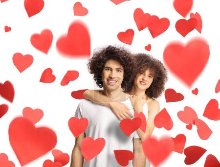 Téléchargez les photos : Jeune homme et femme aux cheveux bouclés dans l'étreinte debout sous des coeurs rouges isolés sur fond blanc - en image libre de droit