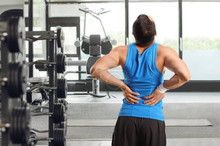 Foto de Vista trasera de un hombre en un gimnasio sosteniendo su rígida columna vertebral - Imagen libre de derechos
