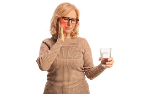 Téléchargez les photos : Femme d'âge moyen avec un mal de dents tenant un verre d'eau isolé sur fond blanc - en image libre de droit