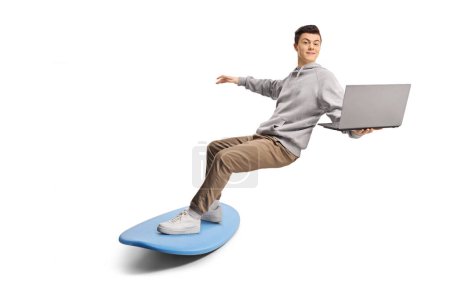 Téléchargez les photos : Guy surfant sur une planche de surf avec des vêtements et tenant un ordinateur portable isolé sur fond blanc - en image libre de droit