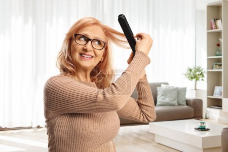 Photo for Beautiful middle aged woman using a wireless hair straightener at home in a living room - Royalty Free Image