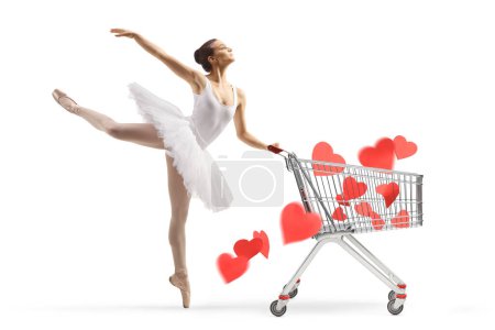 Photo for Full length profile shot of a ballerina in a white tutu dress dancing with hearts in a a shopping cart isolated on white background - Royalty Free Image