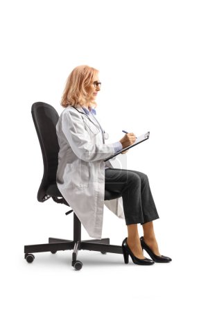 Téléchargez les photos : Médecin femme écrivant un document assis dans une chaise de bureau isolée sur fond blanc - en image libre de droit