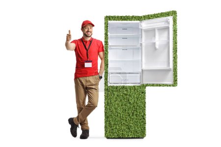 Téléchargez les photos : Assistant de magasin masculin appuyé sur un réfrigérateur vert durable et geste pouces vers le haut isolé sur fond blanc - en image libre de droit