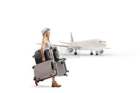 Foto de Foto de perfil completo de una joven caminando cerca de un avión y llevando maletas aisladas sobre fondo blanco - Imagen libre de derechos
