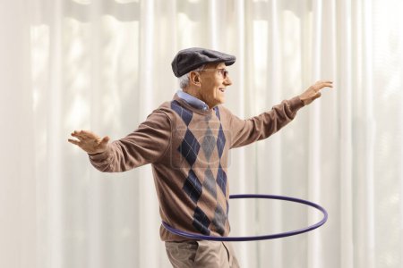 Photo for Cheerful elderly man having fun and spinning a hula hoop at home - Royalty Free Image