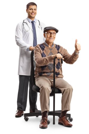 Doctor behind an elderly male patient gesturing thumbs up and sitting in a chair isolated on white background