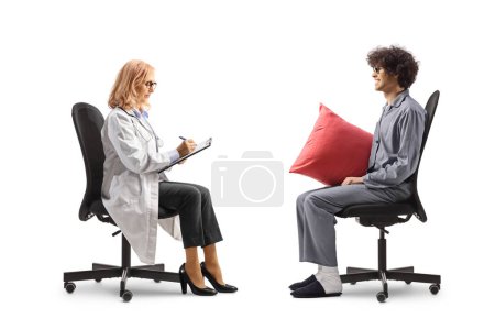 Téléchargez les photos : Homme en pyjama assis et parlant à une femme médecin isolée sur fond blanc - en image libre de droit
