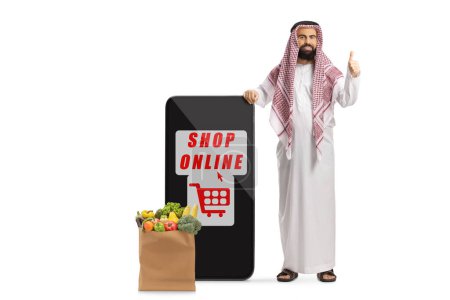 Téléchargez les photos : Satisfait client arabe saudi avec téléphone mobile et application de magasinage en ligne isolé sur fond blanc - en image libre de droit