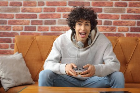 Téléchargez les photos : Portrait d'un gars heureux jouant à des jeux vidéo avec joystick à l'intérieur - en image libre de droit