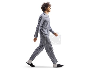 Photo for Full length profile shot of a young man in pajamas and slippers walking isolated on white background - Royalty Free Image