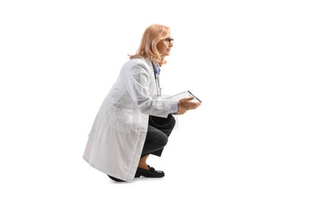Téléchargez les photos : Femme médecin agenouillé et regardant vers le côté isolé sur fond blanc - en image libre de droit