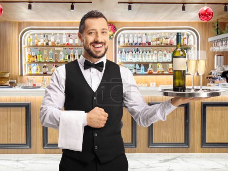 Foto de Camarero frente a un bar sosteniendo una botella de vino en una bandeja - Imagen libre de derechos