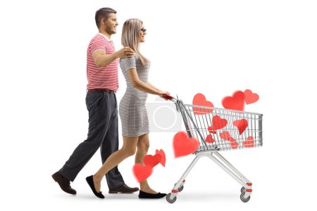 Téléchargez les photos : Photo de profil d'un jeune couple marchant et poussant un chariot avec des cœurs rouges à l'intérieur isolés sur fond blanc - en image libre de droit