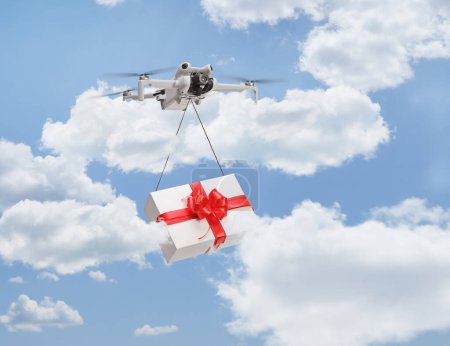 Téléchargez les photos : Drone livrant une boîte cadeau et volant dans un ciel bleu avec des nuages - en image libre de droit