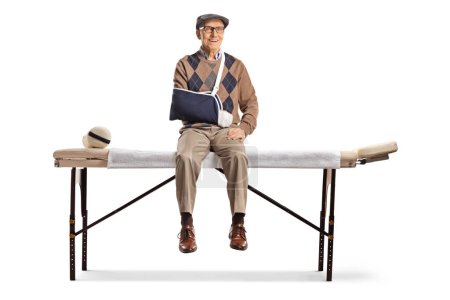 Téléchargez les photos : Homme âgé avec un bras cassé assis sur un lit médical isolé sur fond blanc - en image libre de droit
