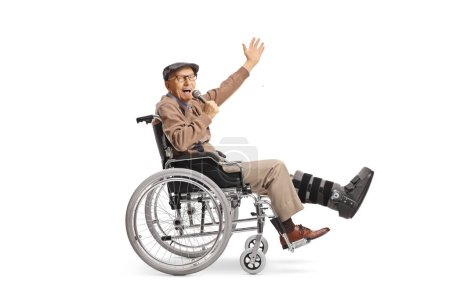 Hombre mayor alegre con una pierna rota en una silla de ruedas sosteniendo un micrófono y cantando aislado sobre fondo blanco