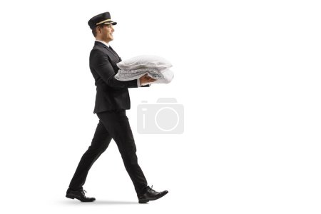 Photo for Full length profile shot of a bellboy carrying a pillow and a duvet isolated on white background - Royalty Free Image
