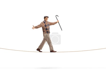Foto de Foto completa de un anciano caballero sosteniendo un bastón y caminando sobre una cuerda aislada sobre fondo blanco - Imagen libre de derechos