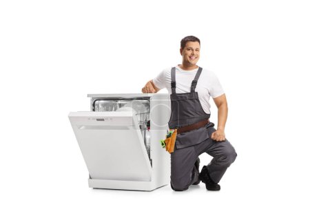 Photo for Repairman kneeling next to a washing dishwasher and looking at camera isolated on white background - Royalty Free Image