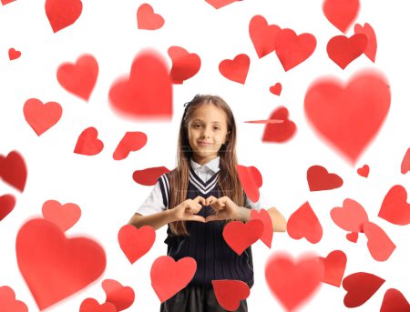 Photo for Schoolgirl gesturing a heart sign with hands and standing under falling hearts isolated on white background - Royalty Free Image
