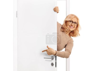 Photo for Middle aged woman peeking from behind a white doorand pointing isolated on white background - Royalty Free Image