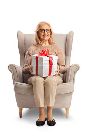 Téléchargez les photos : Femme heureuse assise dans un fauteuil et tenant un cadeau isolé sur fond blanc - en image libre de droit