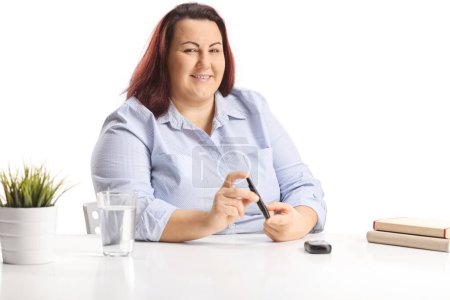 Téléchargez les photos : Corpulent jeune femme assise et poing doigt avec un stylo à insuline et souriant à la caméra - en image libre de droit