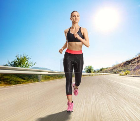 Photo for Young fit woman running on an open road on a sunny day - Royalty Free Image