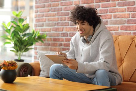 Téléchargez les photos : Un type assis sur un canapé dans un café et utilisant une tablette numérique - en image libre de droit