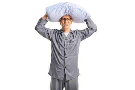 Téléchargez les photos : Homme âgé inquiet en pyjama tenant un oreiller au-dessus de la tête isolé sur fond blanc - en image libre de droit