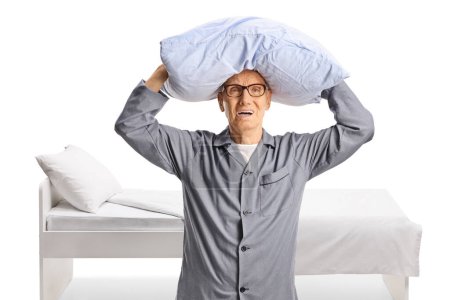 Téléchargez les photos : Homme âgé en colère en pyjama tenant un oreiller au-dessus de la tête isolé sur fond blanc - en image libre de droit