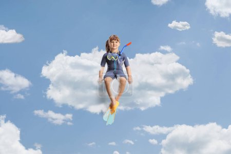 Téléchargez les photos : Petite fille en combinaison avec masque de plongée et palmes flottant sur un nuage dans le ciel - en image libre de droit