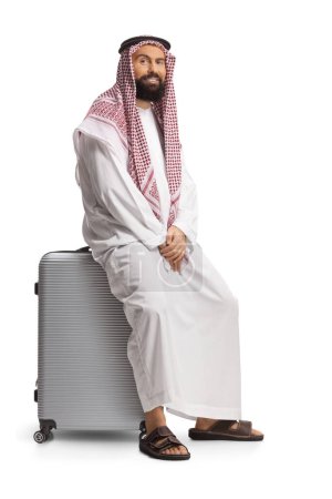 Photo for Saudi arab man sitting on a suitcase and looking at camera isolated on white background - Royalty Free Image