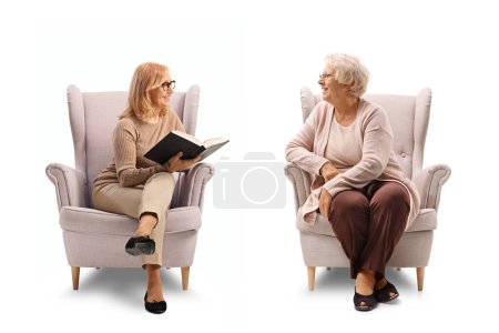 Foto de Mujer de mediana edad y anciana sentada en sillones y sosteniendo un libro aislado sobre fondo blanco - Imagen libre de derechos