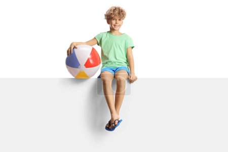 Foto de Niño con una pelota de playa sentado en un panel en blanco aislado sobre fondo blanco - Imagen libre de derechos