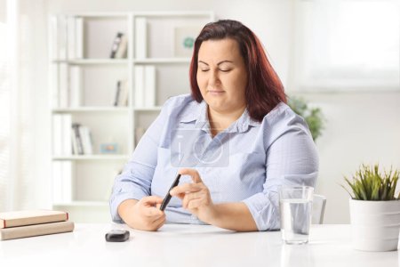 Foto de Mujer joven y corpulenta sentada en casa y usando un dedo pluma de insulina - Imagen libre de derechos